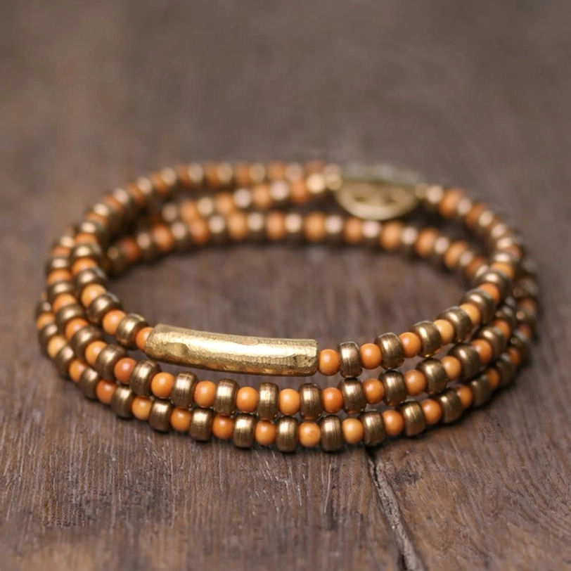 Multi-strand olive pit and copper prosperity bracelet arrangement featuring long brass tube accent, captured from above on natural wood background
