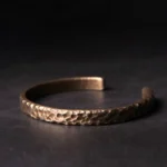 Top-down flat lay of hammered copper adjustable cuff bracelet with bronze tone textured finish