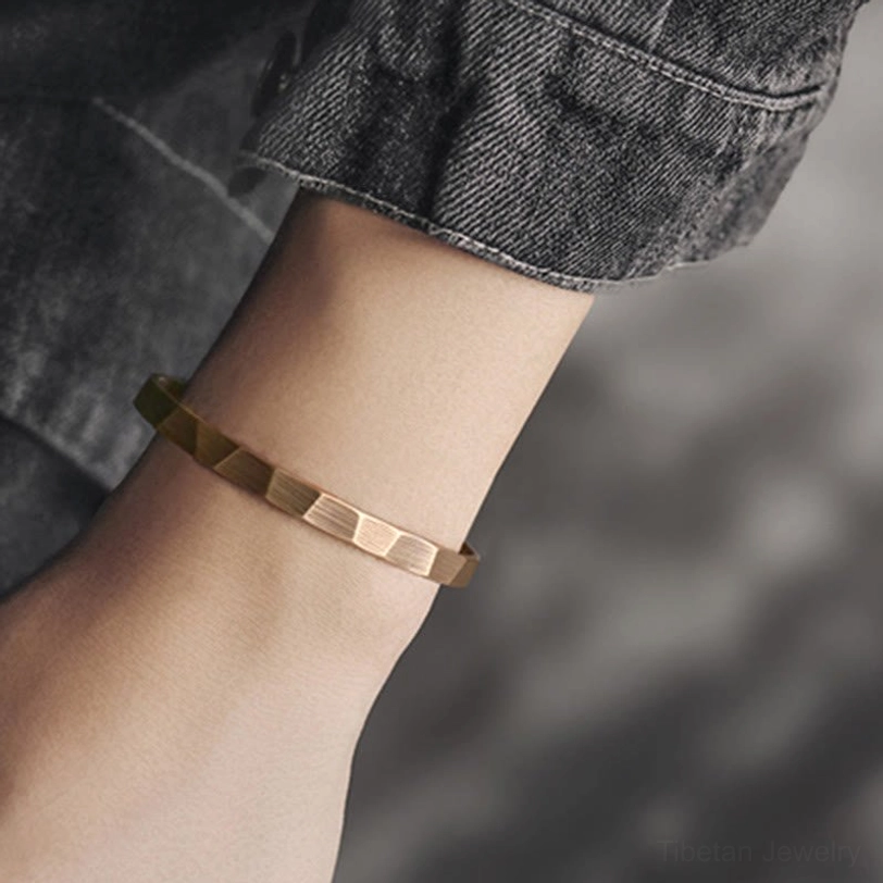 Adjustable copper cuff bracelet worn on wrist with denim, showing slim faceted band fit and bronze patina