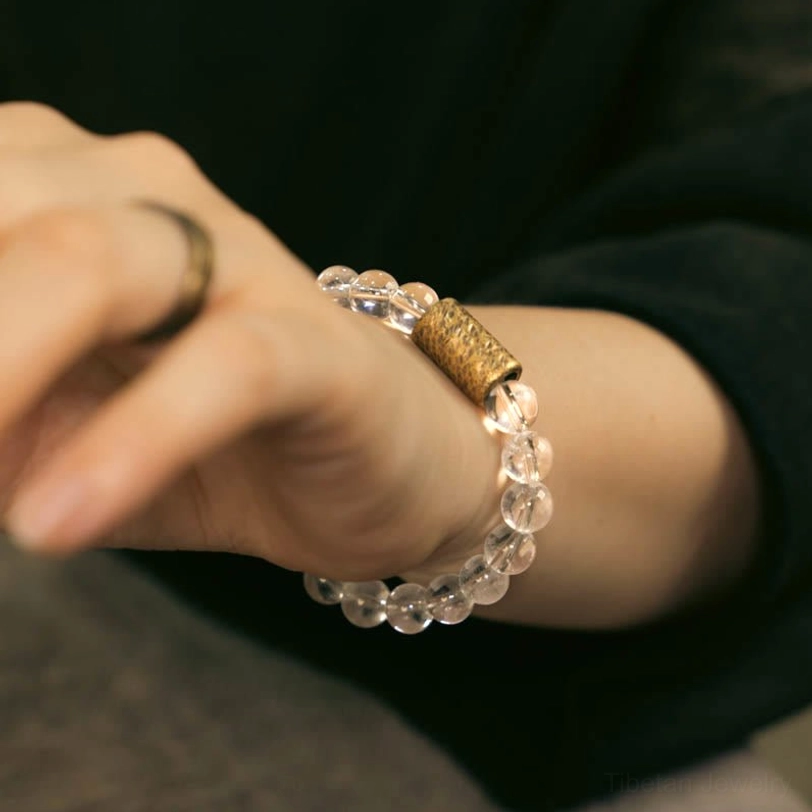 Woman wearing healing crystal bracelet on right wrist with silver ring, styled on dark clothing background