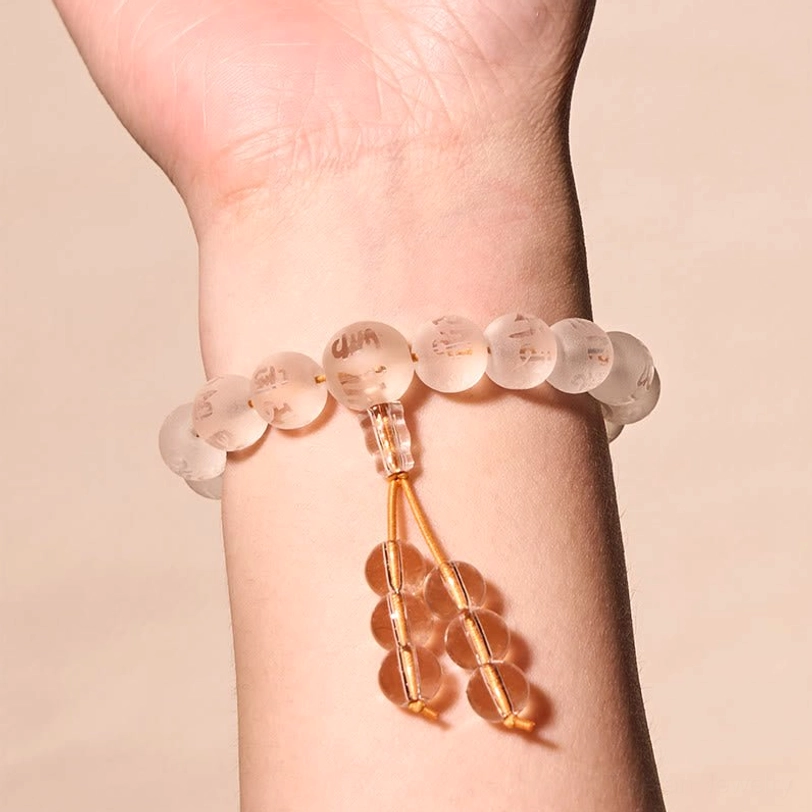 White crystal meditation bracelet worn on left wrist with golden tassel detail