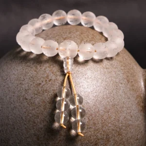 Clear quartz mala bracelet with guru bead and golden cord on ceramic stone display