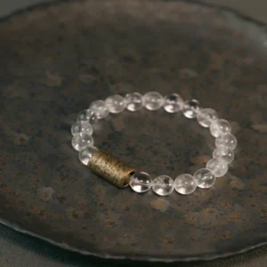 Clear quartz crystal beaded bracelet with copper spacer displayed on dark vintage ceramic plate, overhead flat lay shot