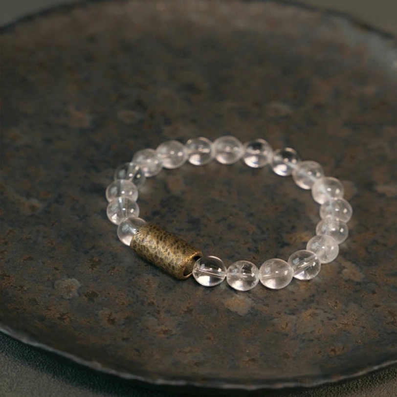 Clear quartz crystal beaded bracelet with copper spacer displayed on dark vintage ceramic plate, overhead flat lay shot