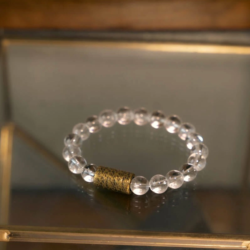 Spiritual protection bracelet featuring clear quartz and copper spacer on mirrored display tray with wooden frame