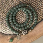 Cyan bodhi seed three-eye dzi triple wrap bracelet with bronze hardware - top down view on wooden surface