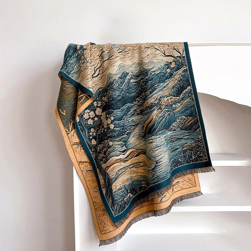 Dark cyan Tibetan landscape shawl with floral mountain pattern on white shelf, side angle showing textured weave and frayed edges