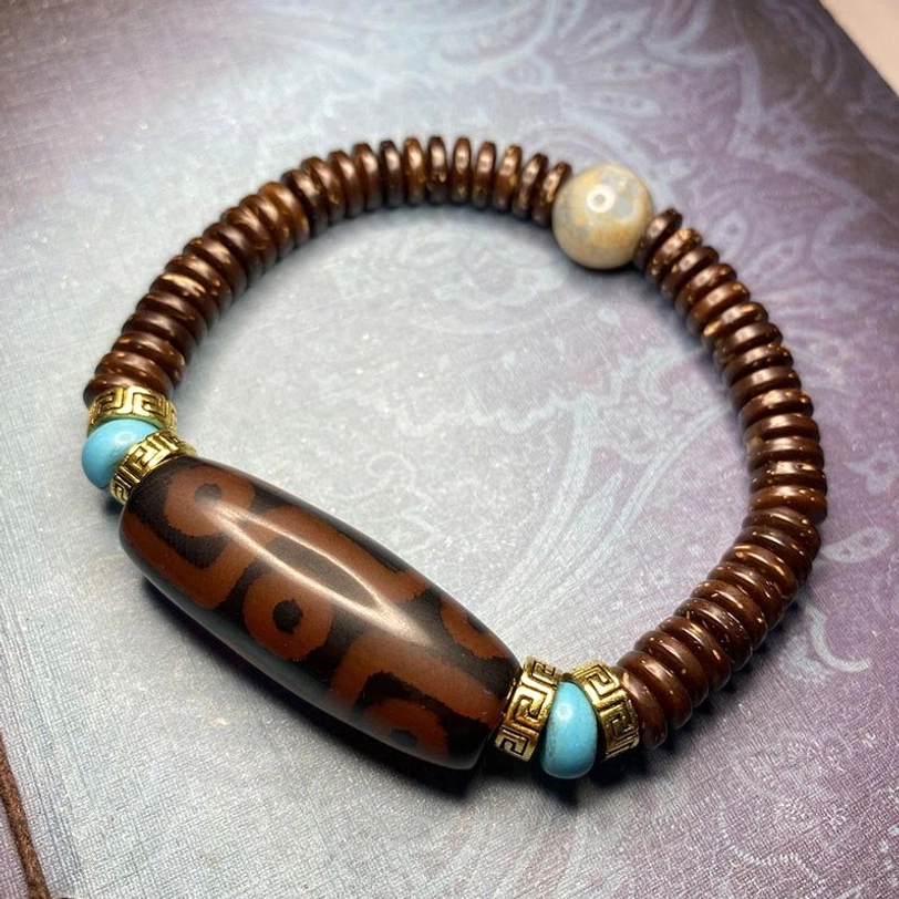 Dark red nine-eye dzi bead bracelet with light jade accent stone, turquoise and metal spacers on light purple textured background