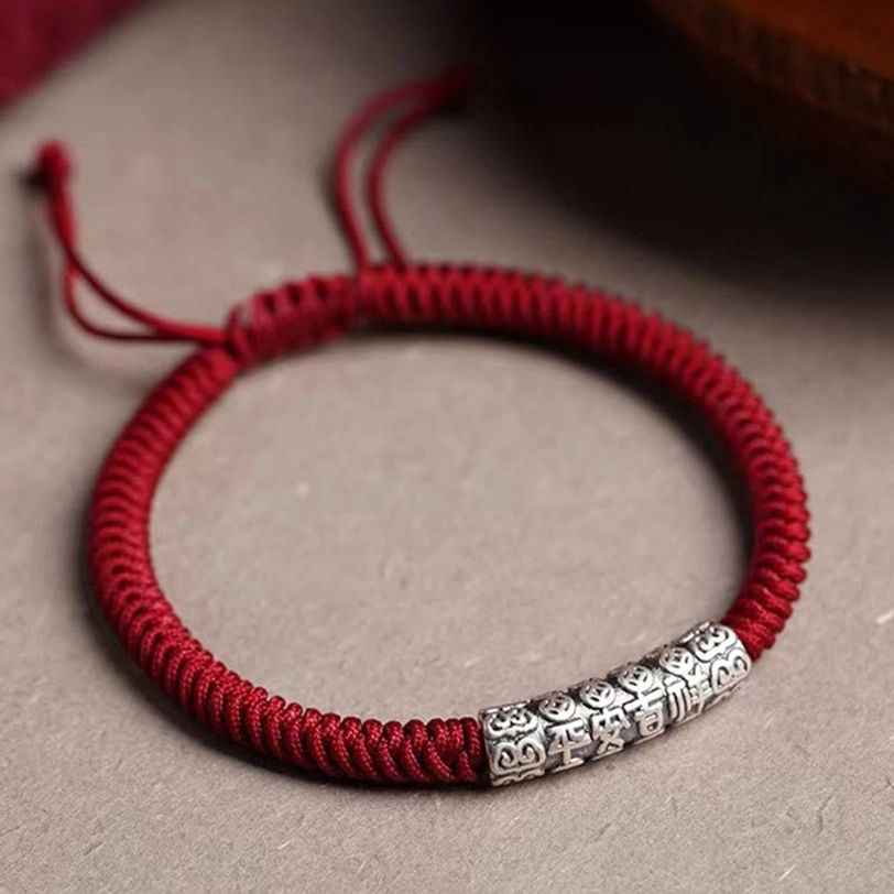 Deep burgundy dark red Tibetan luck rope bracelet with long engraved silver mantra charm, close-up top-down view