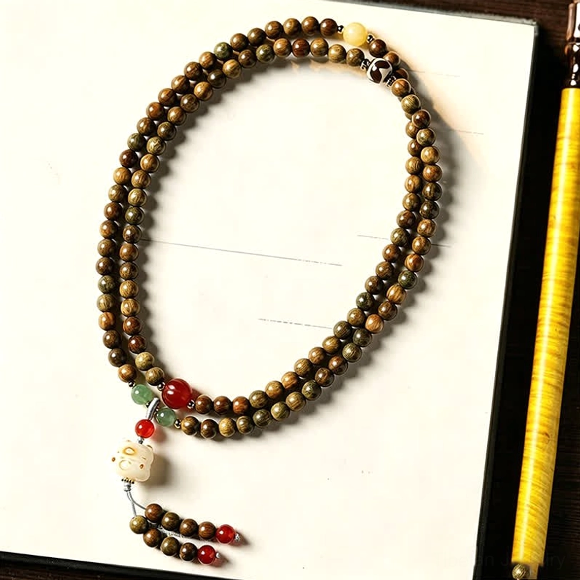 Dark brown sandalwood mala bracelet with cat tassel pendant, styled with pen and wooden plaque on desk setup