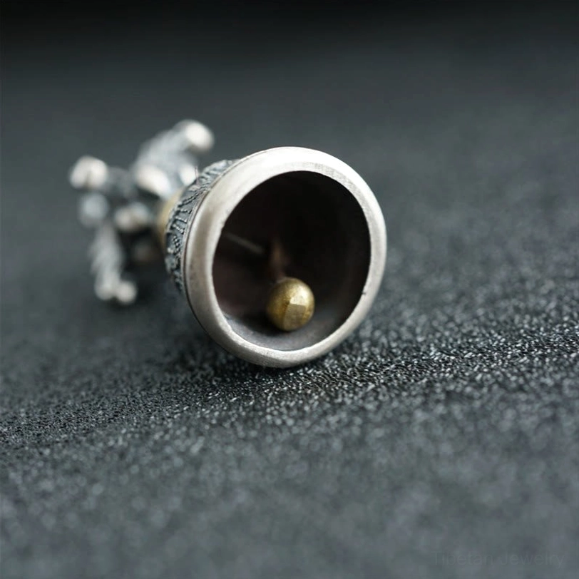 Overhead close-up of dorje bell pendant showing brass clapper inside silver bell chamber, detailed craftsmanship view