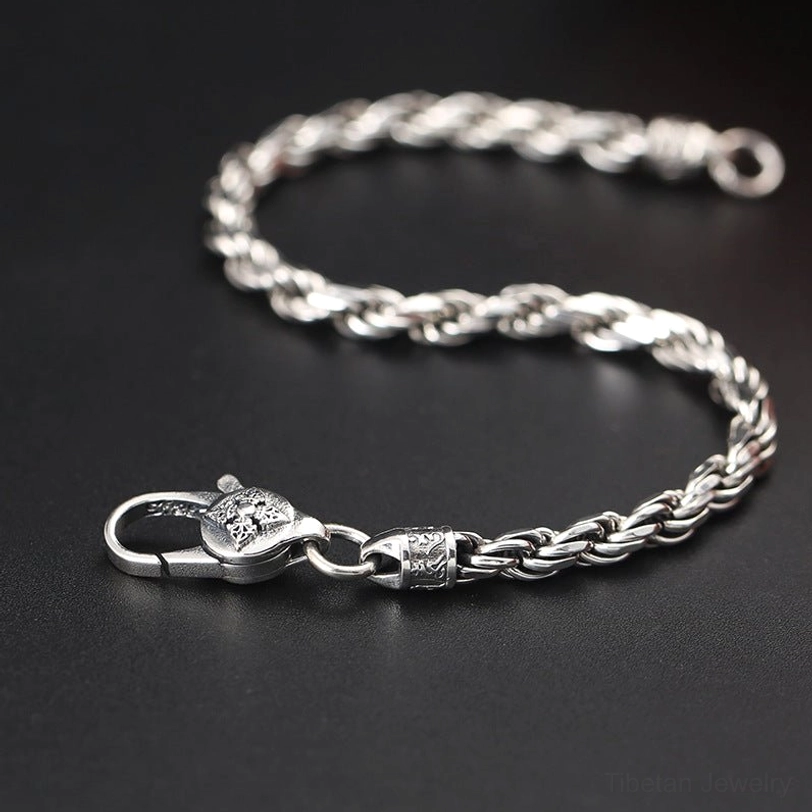 Close-up side view of Double Dorje Vajra sterling silver bracelet showing twisted rope chain and carved decorative segments on dark background