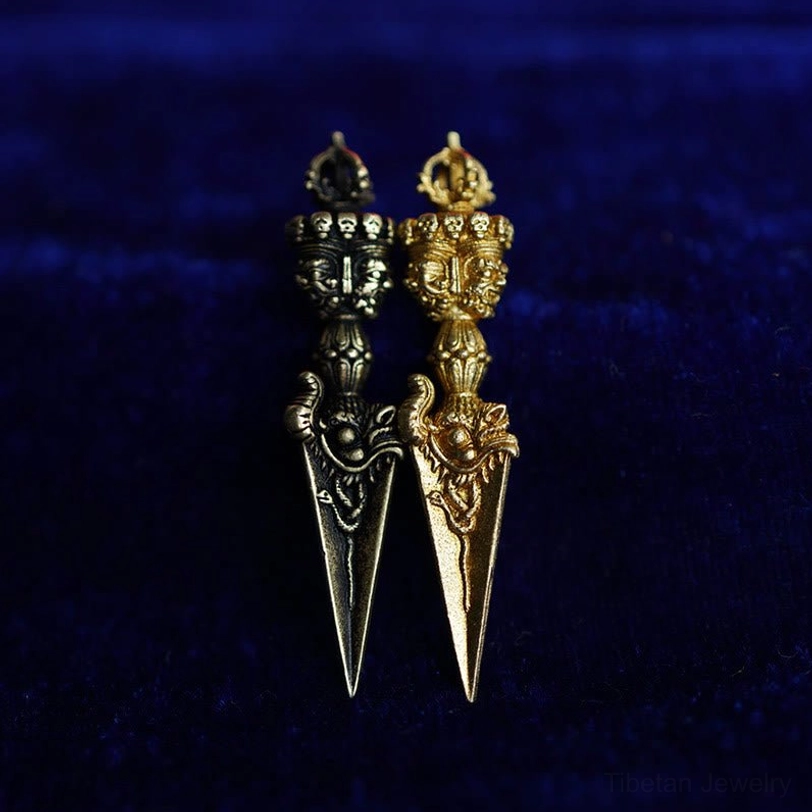 Two Tibetan Dorje Vajra pendants comparison - one black bronze and one bright gold-tone, both with identical sacred carved designs on blue velvet