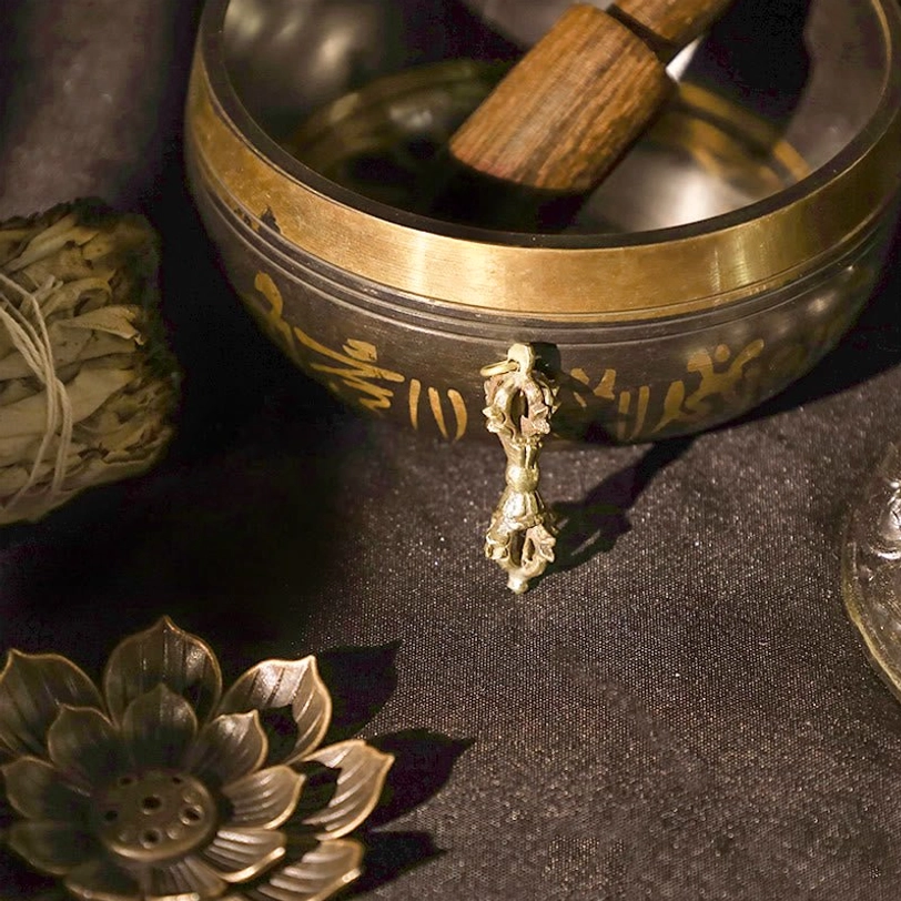 Single dorje vajra pendant paired with engraved singing bowl and lotus decor - traditional Tibetan Buddhist spiritual objects on dark cloth