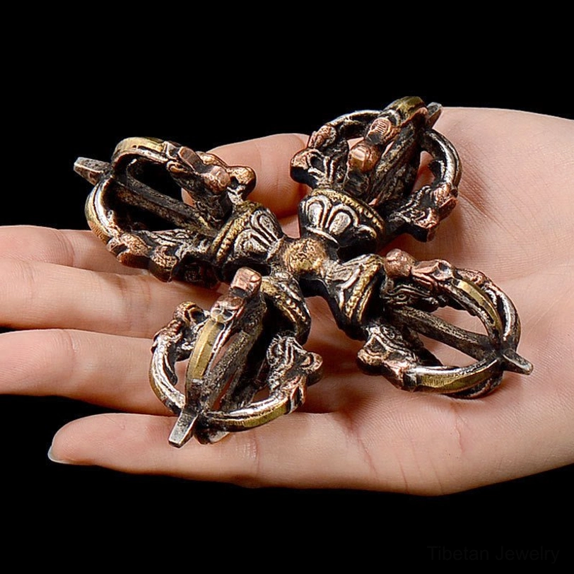 Tibetan double dorje vajra held in human palm showing scale and ornate aged metal finish with carved religious details