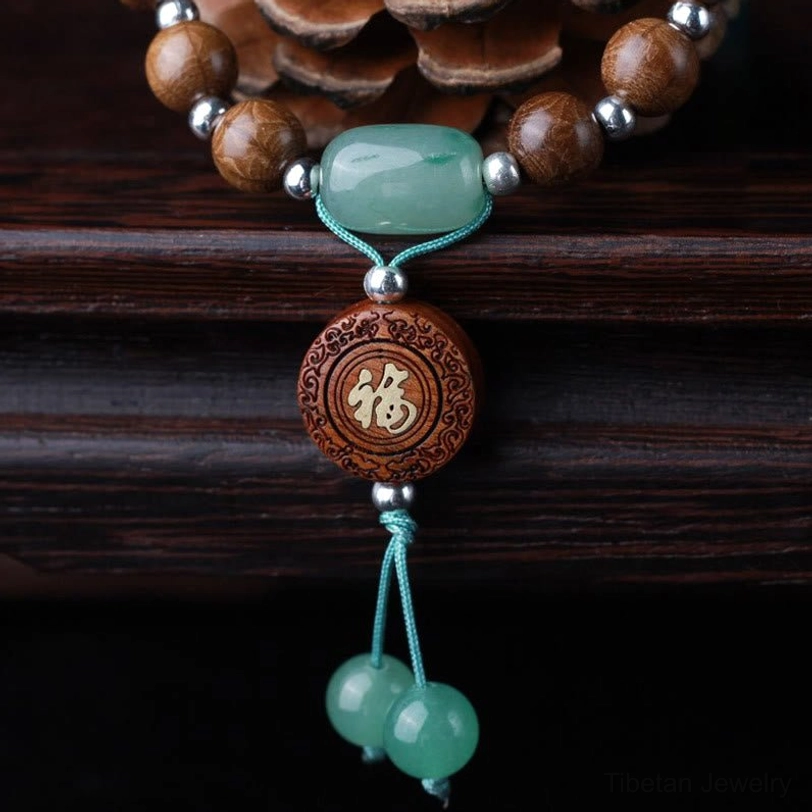 Close-up overhead view of sacred dragon wood bracelet with six-line beads, green barrel jade, carved fu charm, and tassel accents