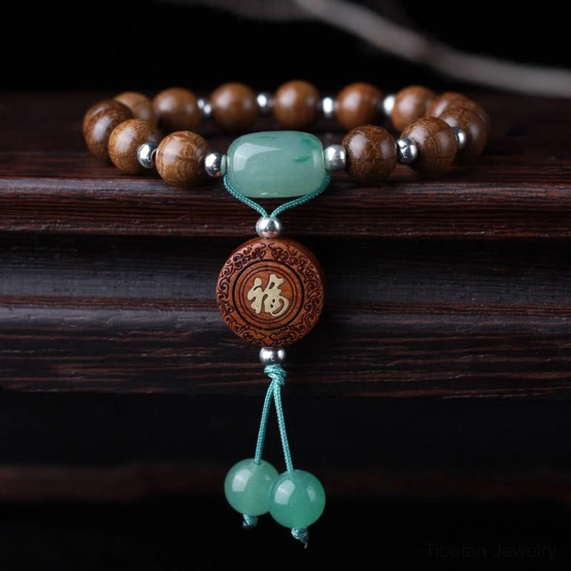 Dragon wood Tibetan blessing bracelet with om mani padme hum beads, green jade accents, and silver spacers displayed on dark wood surface