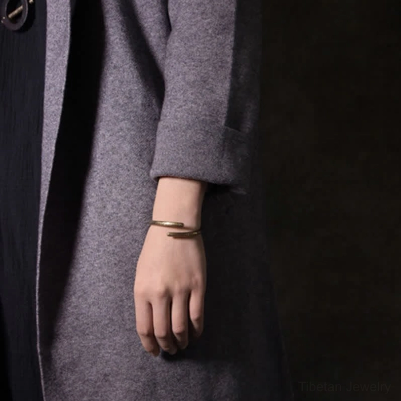 Two stacked copper cuff bracelets worn on both wrists, antique gold finish with grey coat