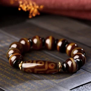 Tibetan dzi agate beaded bracelet overhead view showing round striped agate beads and central nine-eye dzi bead on dark vintage paper