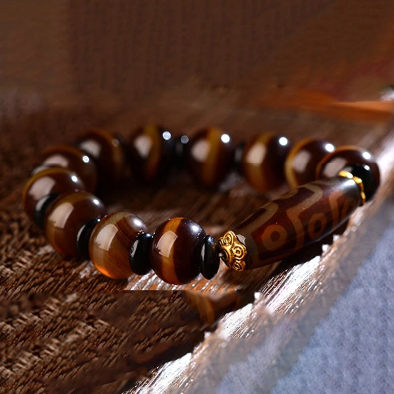 Tibetan dzi agate bracelet low-angle flat lay on wooden textured surface displaying traditional dzi bead pattern with gold spacers