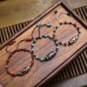 Three handmade Dzi bead protection bracelets in Coconut, South Red Agate, and Turquoise styles with braided cord and adjustable knots