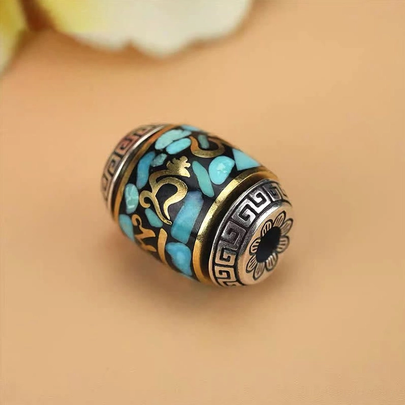 Single barrel Tibetan Dzi bead pendant macro shot displaying turquoise inlay, hand-painted gold Sanskrit markings and silver decorative edges
