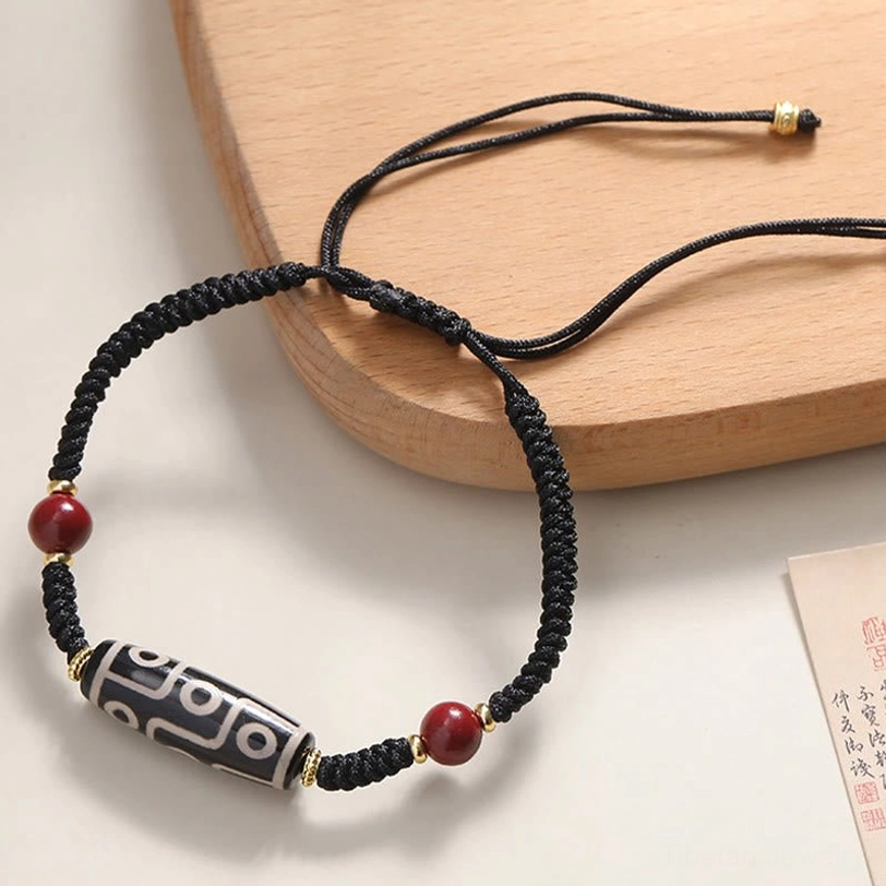 Adjustable nine-eye dzi bead bracelet close-up showing braided cord and sliding knot on vintage wooden tray