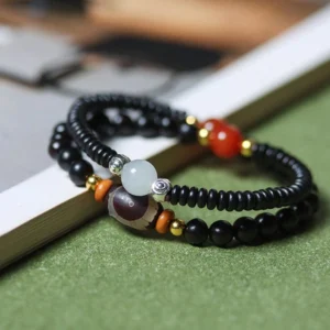 Close-up side view of Dzi bead protection bracelet showing black ebony beads, red agate accents, and metal spacers on green fabric