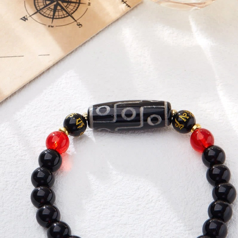 Nine-eye dzi bead bracelet prominent detail with red and gold accent beads on compass background