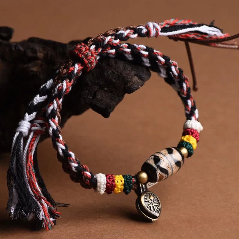 Single-strand Tibetan Dzi bead bracelet with mixed-color woven rope, round copper pendant, and tasseled ends on dark background