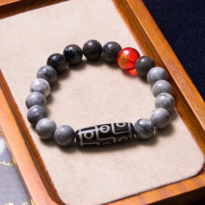 Tibetan nine-eye dzi bracelet on elegant wooden tray with gold-printed red accent bead and authentic Himalayan sacred dzi stone