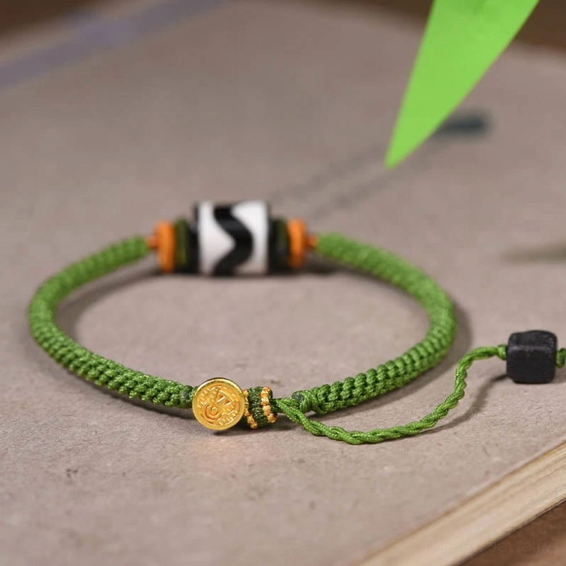 Tibetan dzi bead bracelet with gold charm detail and green woven rope, top-down view