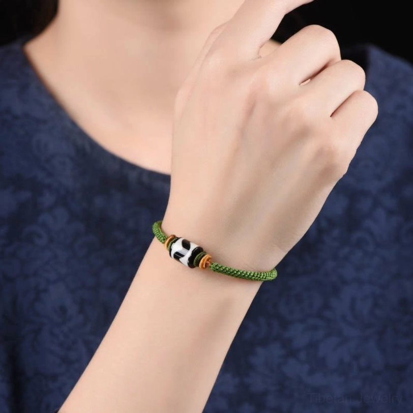 Worn tibetan dzi bead protection bracelet on wrist with dark blue clothing background