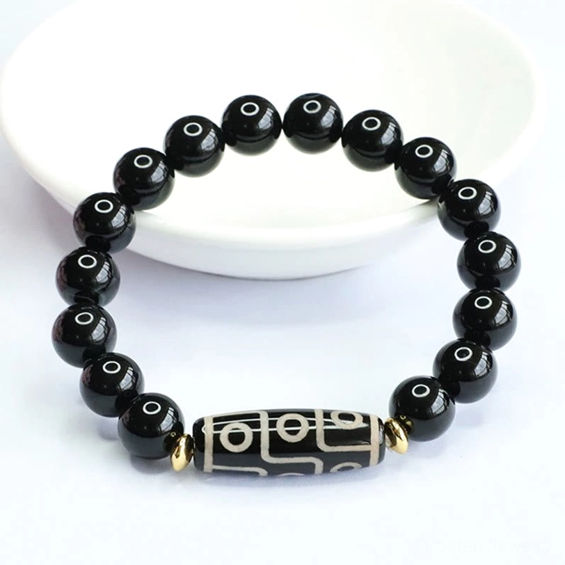Side overhead view of nine-eye dzi protection bracelet on white plate showing smooth black round beads with gold spacers and dzi centerpiece