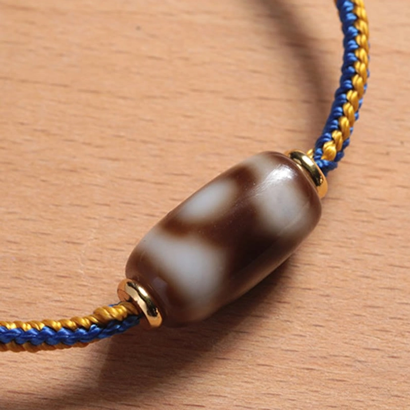 Tibetan Dzi bead bracelet polished finish, close-up showing cylindrical bead with gold end caps and premium braided cord
