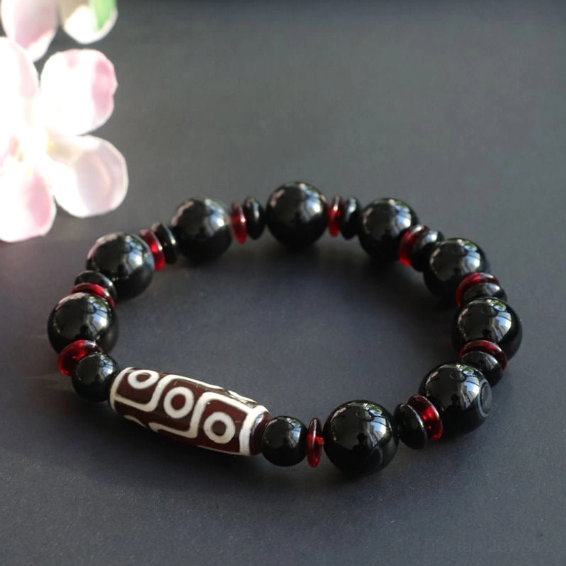 Hand-painted Nine-Eye Dzi Bead bracelet with black onyx stones and red spacers displayed with pink floral decoration, emphasizing spiritual and prosperity energy