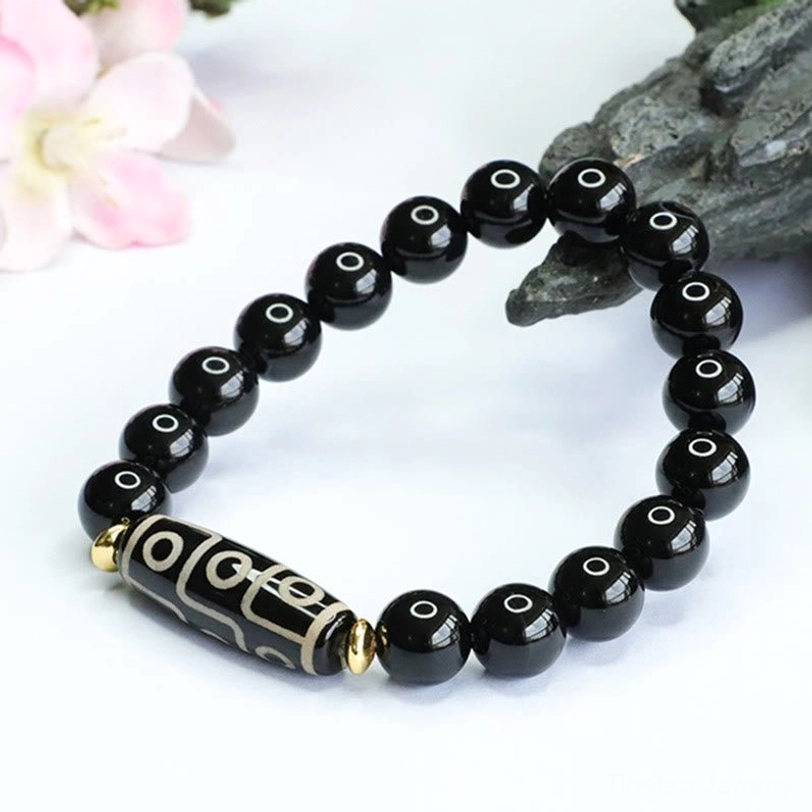 Side angled photography of nine-eye dzi bead black onyx power bracelet showing patterned dzi focal stone detail
