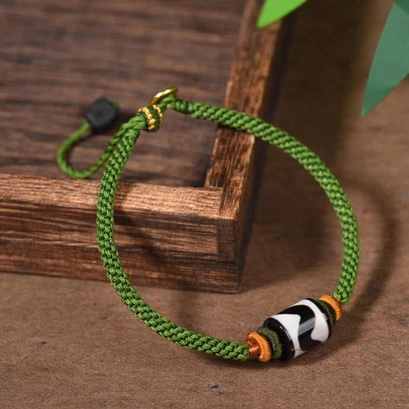 Side view of handcrafted dzi bead protection bracelet with adjustable black slide clasp and woven green cord