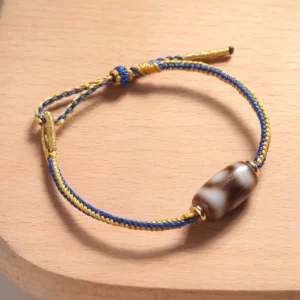 Three-eye Dzi bead bracelet side view, detailed look at cylindrical agate bead with authentic eye patterns and gold hardware