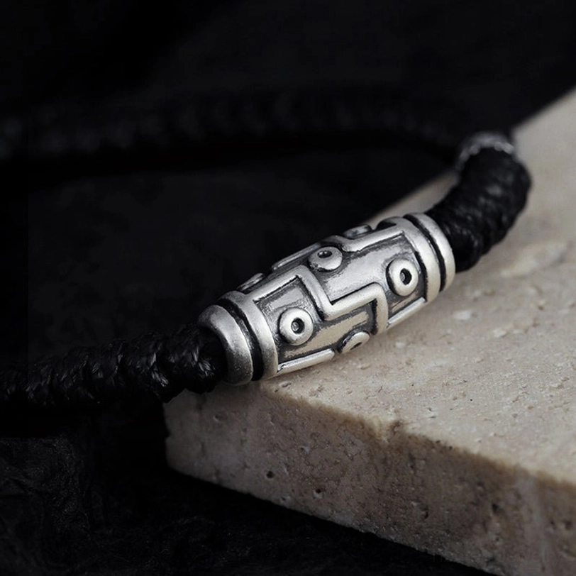Tibetan nine-eye dzi bead bracelet side view on stone surface, vintage silver finish with decorative fastener and rope
