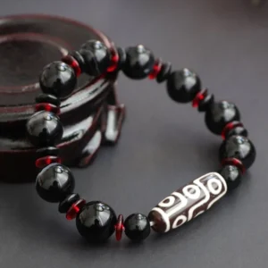 Top view of Nine-Eye Dzi Bead wealth protection bracelet featuring central hand-painted Dzi bead surrounded by polished black onyx gemstones and red glass spacers
