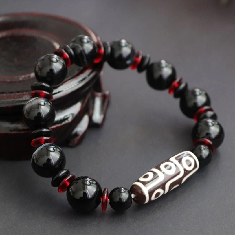 Top view of Nine-Eye Dzi Bead wealth protection bracelet featuring central hand-painted Dzi bead surrounded by polished black onyx gemstones and red glass spacers