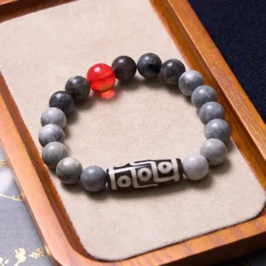 Tibetan nine-eye dzi protection bracelet displayed on wooden velvet tray, featuring grey stone beads and sacred nine-eye dzi focal bead