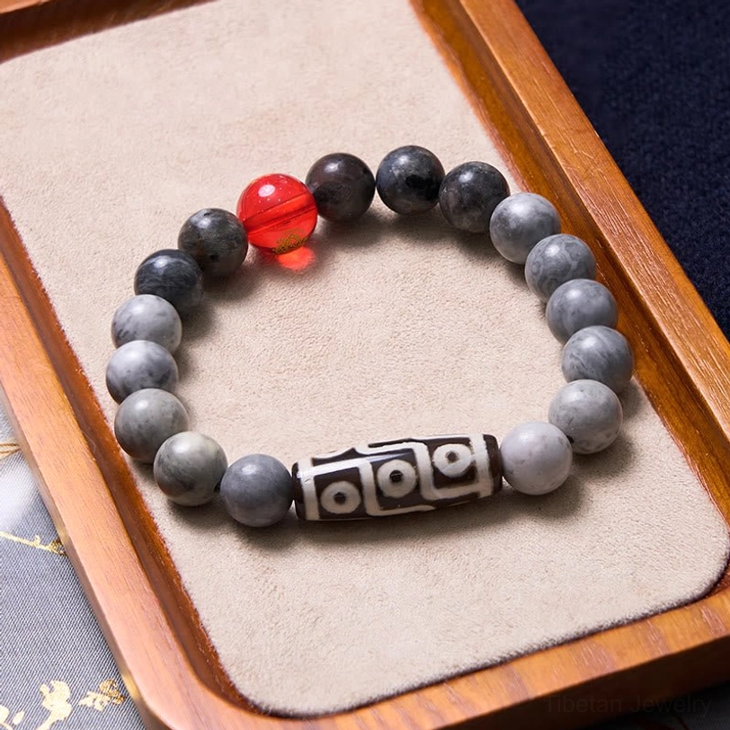 Tibetan nine-eye dzi protection bracelet displayed on wooden velvet tray, featuring grey stone beads and sacred nine-eye dzi focal bead