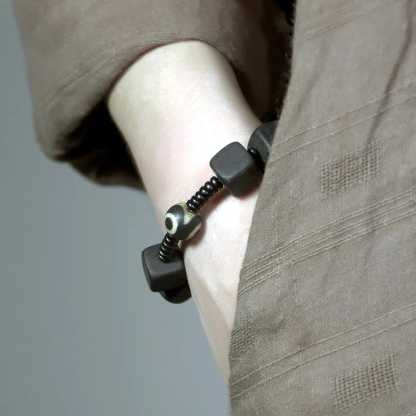 Nine-eye dzi bead bracelet worn on wrist close-up showing matte black ebony wood square beads and protective amulet bead detail