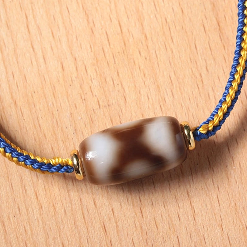 Close-up macro shot of three-eye Dzi bead bracelet, highlighting natural agate texture and gold metal spacers