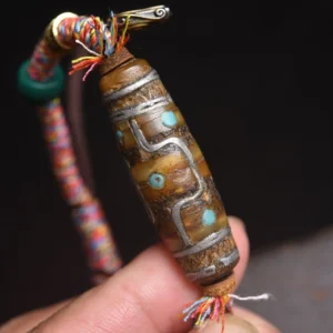 Close-up macro view of authentic Tibetan Dzi bead with silver inlay patterns and turquoise accents held in hand