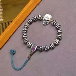 Tibetan Dzi Bead Lord of Corpse Forest protection bracelet overhead view with nine-eye beads, skull charm, and blue tassel