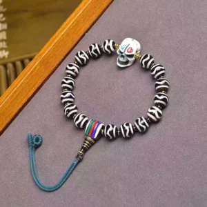 Tibetan Dzi Bead Lord of Corpse Forest protection bracelet overhead view with nine-eye beads, skull charm, and blue tassel