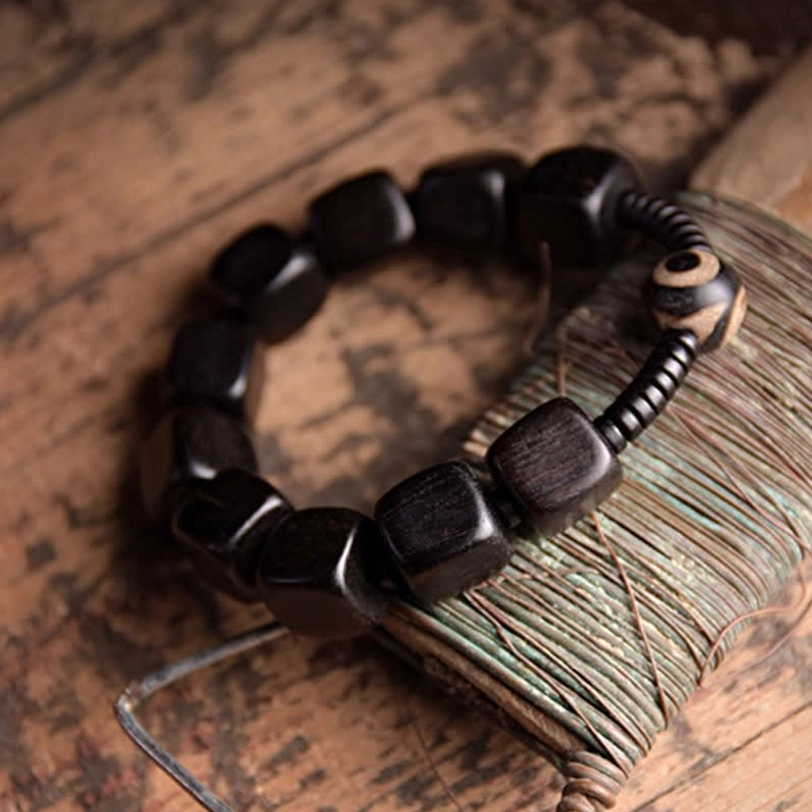 Spiritual ebony wood dzi bracelet three-quarter view displaying square dark wood beads with eye-motif dzi accent on vintage sewing spool